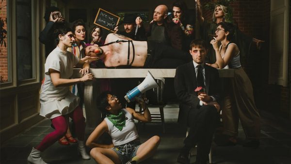 Roomful of Teeth promotional photo of several people gathered around a man on a table