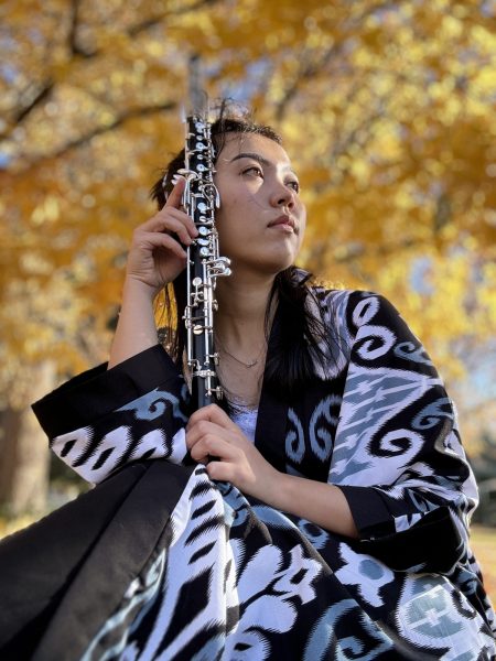 Madina Rashidova picture in a white patterned black dress with her oboe beside her face.