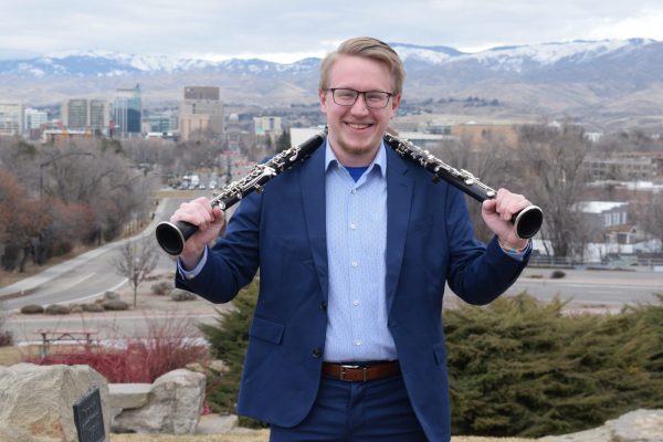 Peter Hansen pictured in front of mountains with two clarinets, one on each shoulder.