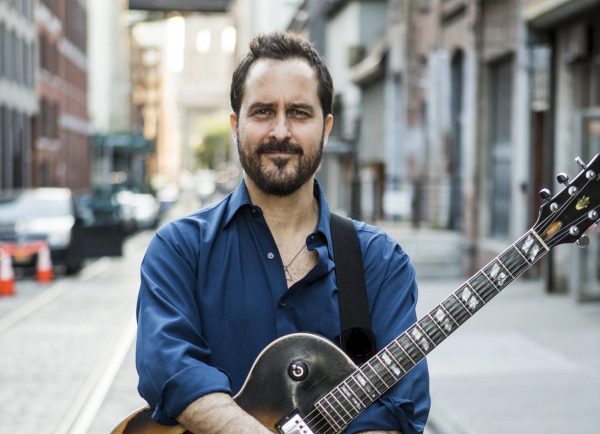 2026 Guest Artist Jonathan Kriesberg, promotional photo in a blue shirt and guitar on a city street